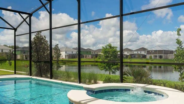 A swimming pool with a hot tub, surrounded by a metal fence, with a view of houses and a body of water in the background. - 10BD Bella Vida Modern Home Private Pool (BV 4456) (Kissimmee)