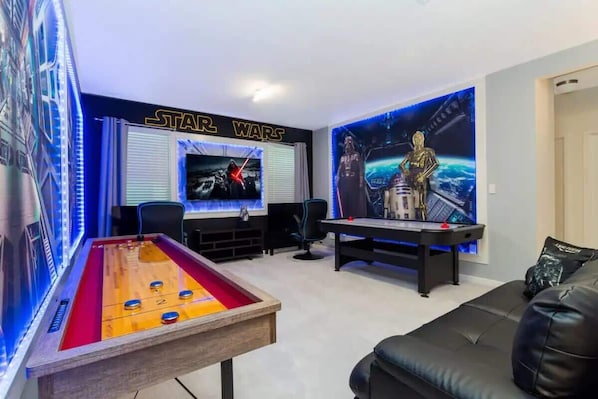 A room with a pool table, a sofa, Star Wars-themed decor, and a TV screen.