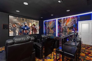 A movie theater with a large screen, black leather seating, and colorful wall art.