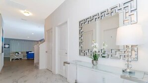 A modern interior with a glass console table, a decorative mirror, and a potted plant.