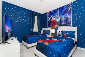 A bedroom with two beds, star-patterned walls, and a large Disney-themed poster.
