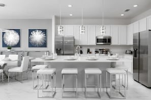 Una cocina moderna con armarios blancos, electrodomésticos de acero inoxidable y taburetes de bar.