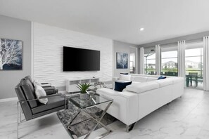 Uma sala de estar moderna com um sofá branco, uma mesa de centro de vidro, um sofá preto, uma TV de tela plana e obras de arte nas paredes.