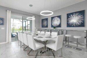 Uma área de jantar moderna com divisória de vidro, cadeiras brancas, piso de mármore e três luminárias no teto.
