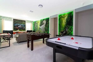 A room with a foosball table, a pool table, and a sofa.