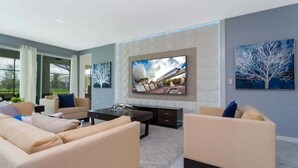 Ein modernes Wohnzimmer mit einem großen Flachbildfernseher an der Wand, beigefarbenen Sofas, einem Couchtisch und einem Kamin.