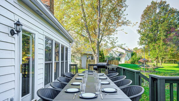 A long dining table set for a meal with chairs, a grill, and a well-maintained garden in the background. - HUGE Home w/ Movie Room, Pool Table & Arcade Games (Indianapolis)