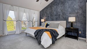 A bedroom with a bed, two bedside tables, a ceiling fan, and a view of trees through the window. - HUGE Home w/ Movie Room, Pool Table & Arcade Games (Indianapolis)