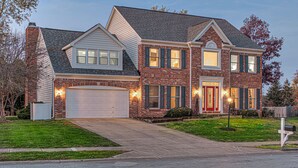 A two-story house with a garage, brick exterior, and a well-maintained lawn. - HUGE Home w/ Movie Room, Pool Table & Arcade Games (Indianapolis)