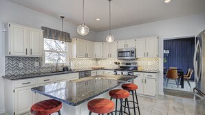 A modern kitchen with white cabinets, a large island with stools, a microwave, and a stove. - HUGE Home w/ Movie Room, Pool Table & Arcade Games (Indianapolis)