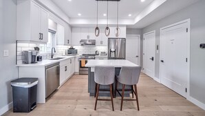 A modern kitchen with white cabinetry, stainless steel appliances, and a central island with bar stools. - Cottage featuring Lake view balcony, private elevator and 3 en-suites! (Fort Erie)