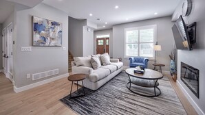 A modern living room with a grey sofa, a round coffee table, and a fireplace. - Cottage featuring Lake view balcony, private elevator and 3 en-suites! (Fort Erie)