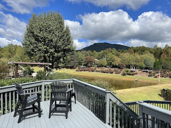 A deck with two Adirondack chairs overlooking a pond and a mountainous landscape.