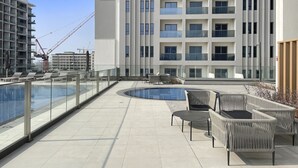 Un área de piscina en la azotea con sillones y vistas a un edificio moderno.