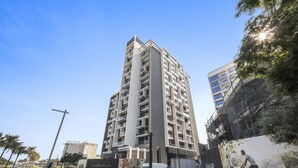 Un edificio alto con varios pisos, una entrada destacada y un gran cartel publicitario a la derecha.