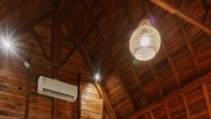 Une chambre dans un chalet en bois, avec deux lits, un luminaire suspendu, un appareil de climatisation et une table de chevet avec une lampe.