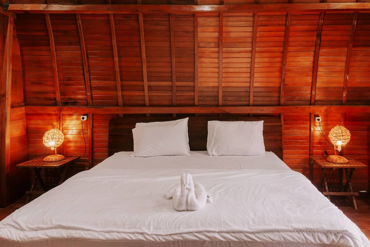 Una habitación con paneles de madera, una cama grande, dos almohadas blancas y dos mesitas de noche con lámparas.