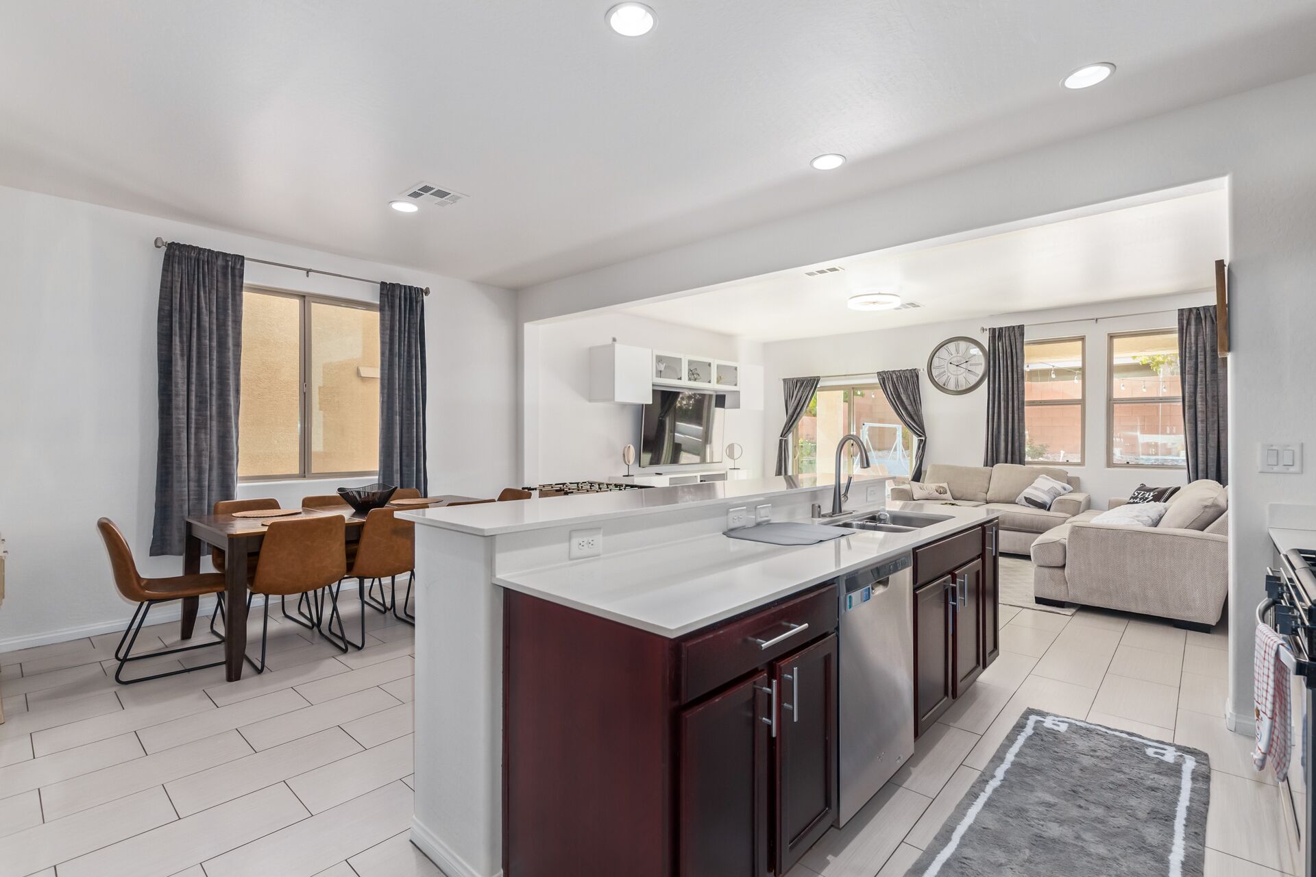 A modern kitchen with a central island, dining area with chairs, and a living space with a sofa and a clock on the wall.