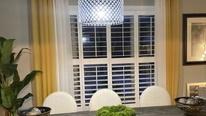 A dining area with a table, chairs, a bench, a hanging light fixture, and a window with blinds.