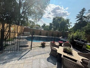 A backyard with a swimming pool, a fenced patio area, and outdoor furniture. - Comfortable & Bright 4BD Stay Near Airport & Downtown Toronto w/opt pool access  (Mississauga)