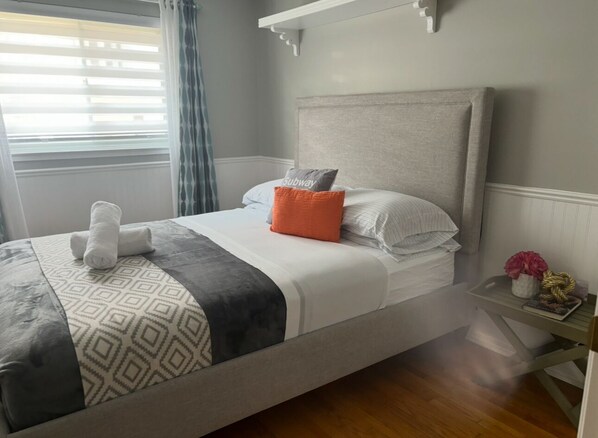 A neatly made bed with a patterned blanket, a grey headboard, and a bedside table with a vase and a book.