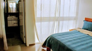 A bedroom with a bed, a nightstand, and a window with sheer curtains.