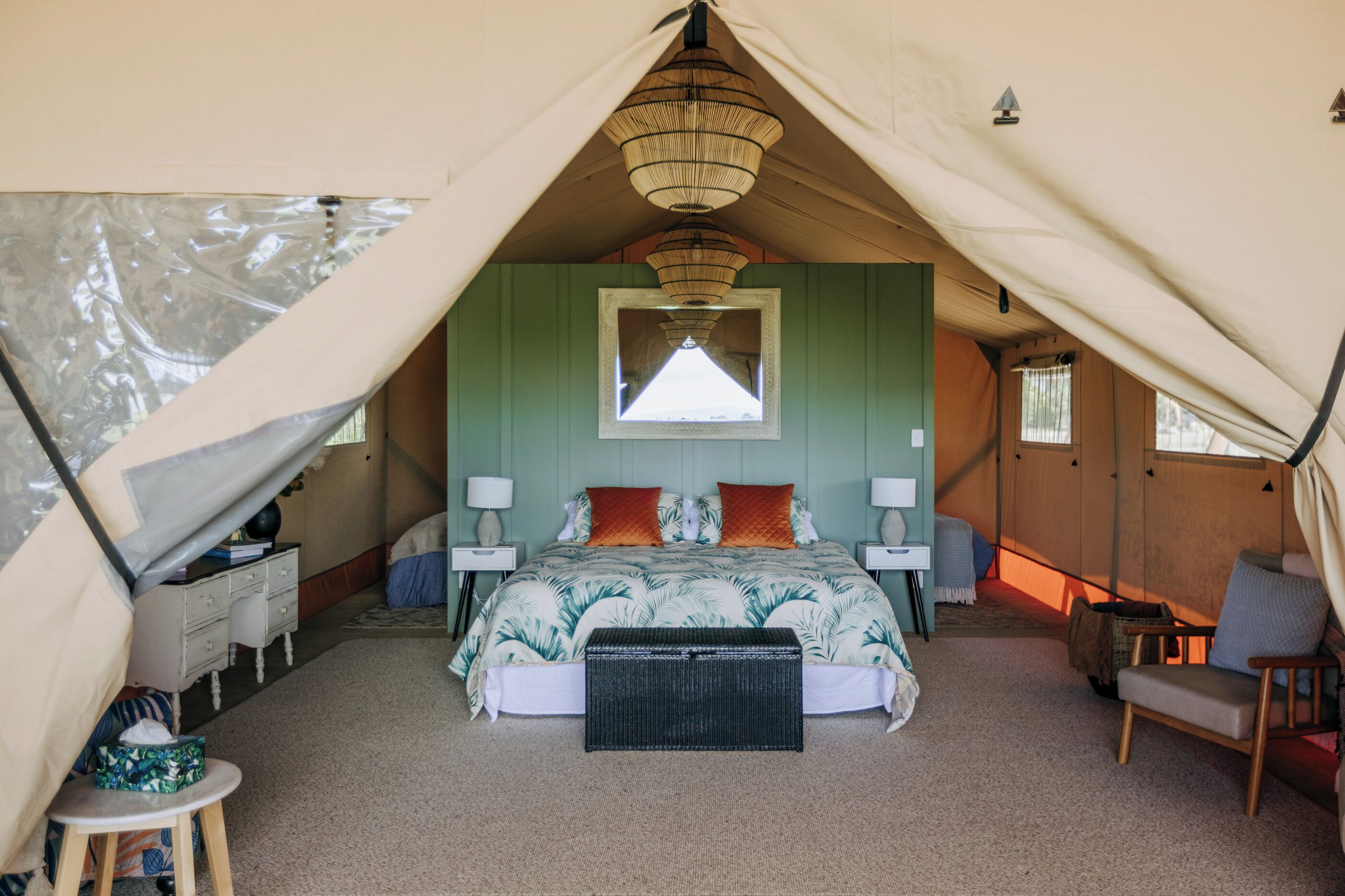 A tented accommodation room with a bed, bedside tables, lamps, and a chair.