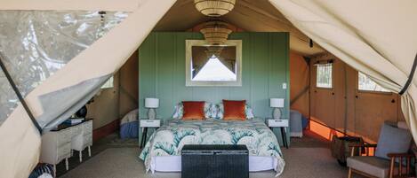 A tented accommodation room with a bed, bedside tables, lamps, and a chair.