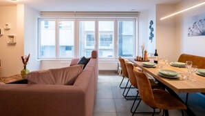 A modern dining area with a long table, multiple chairs, and a sofa. - La Marée with parking & lateral seaview by Interhome (Blankenberge)