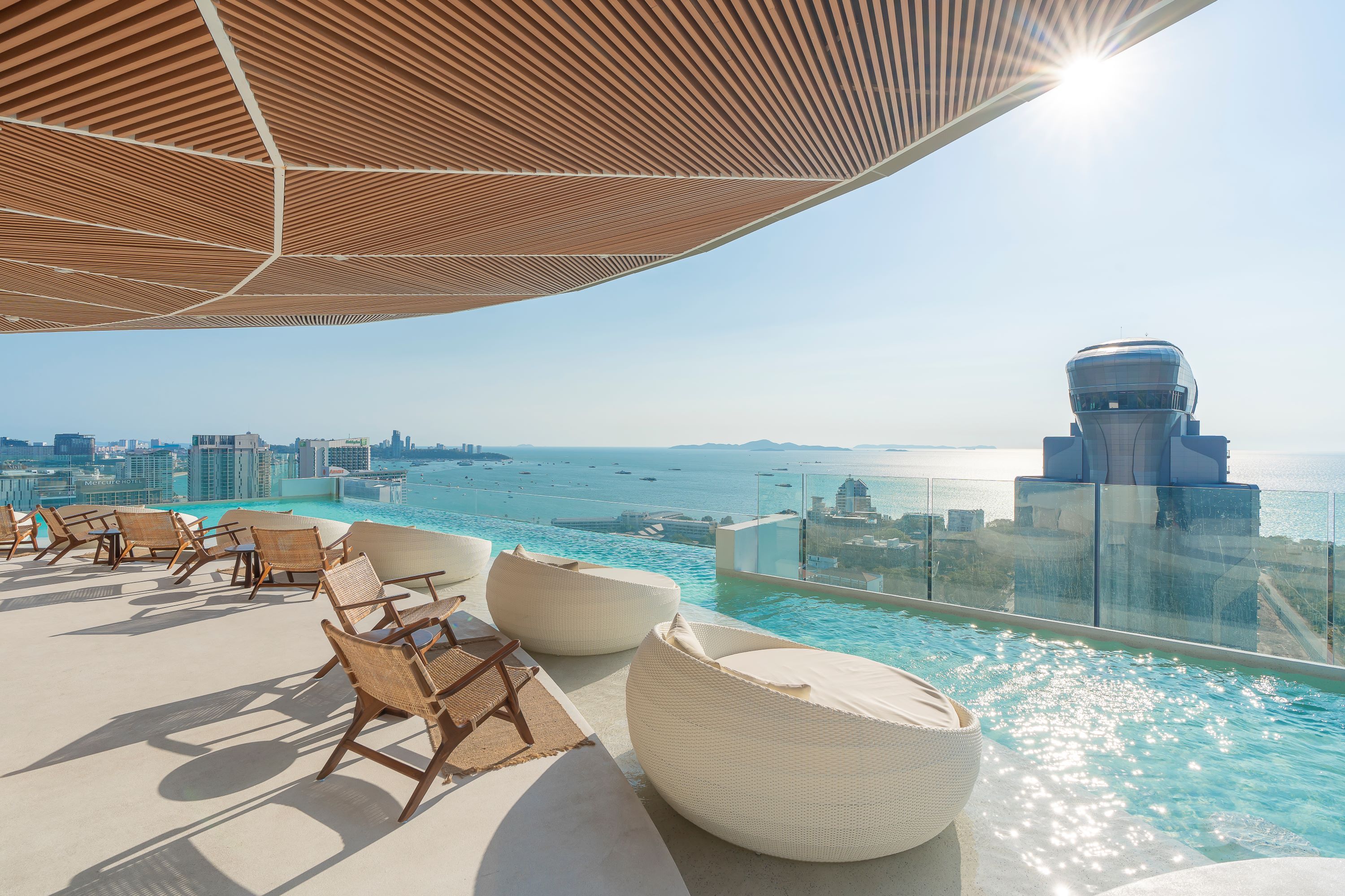 A rooftop infinity pool with lounge chairs and a view of the sea and cityscape.