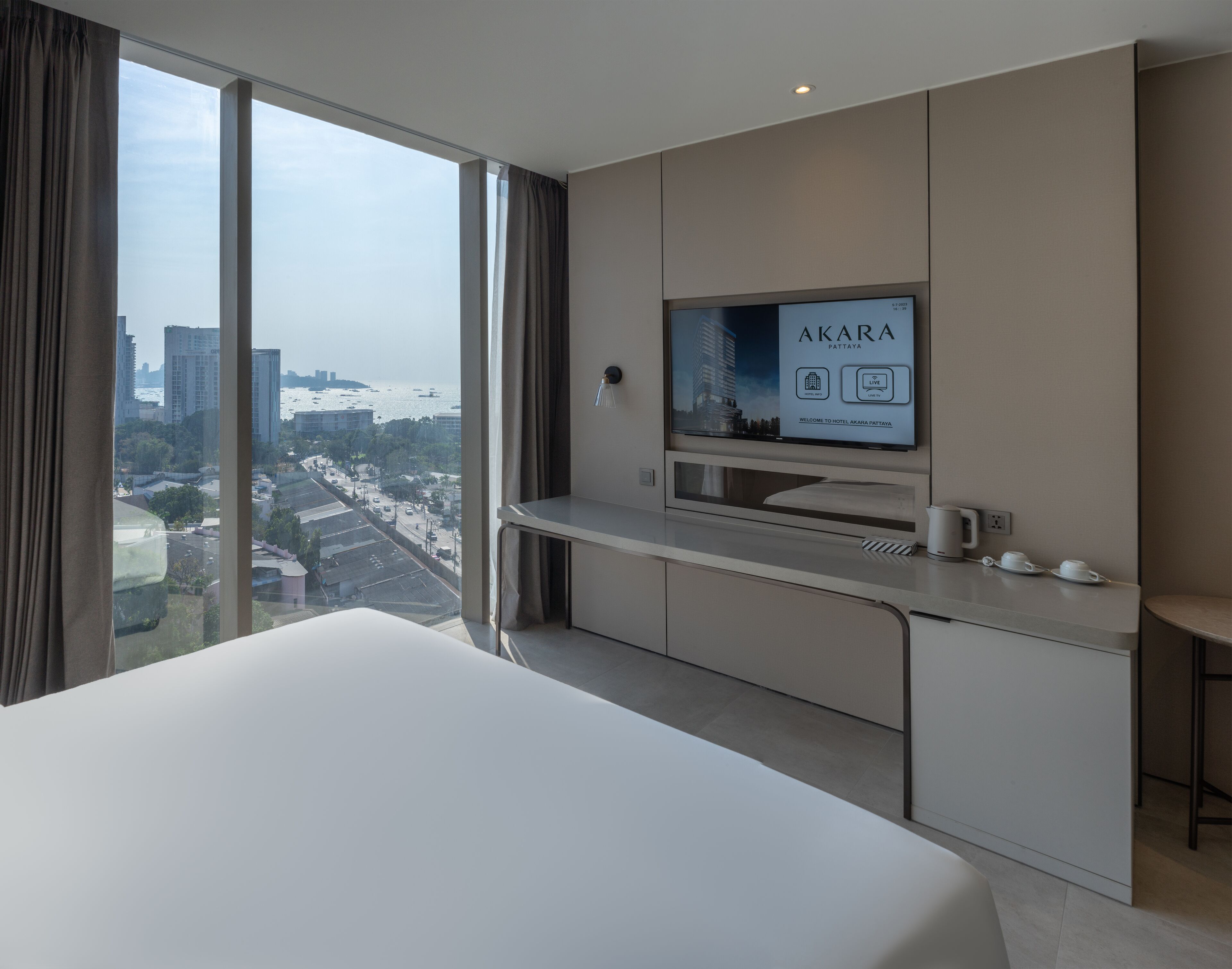 A modern hotel room with a large bed, a TV mounted on the wall, and a city view.