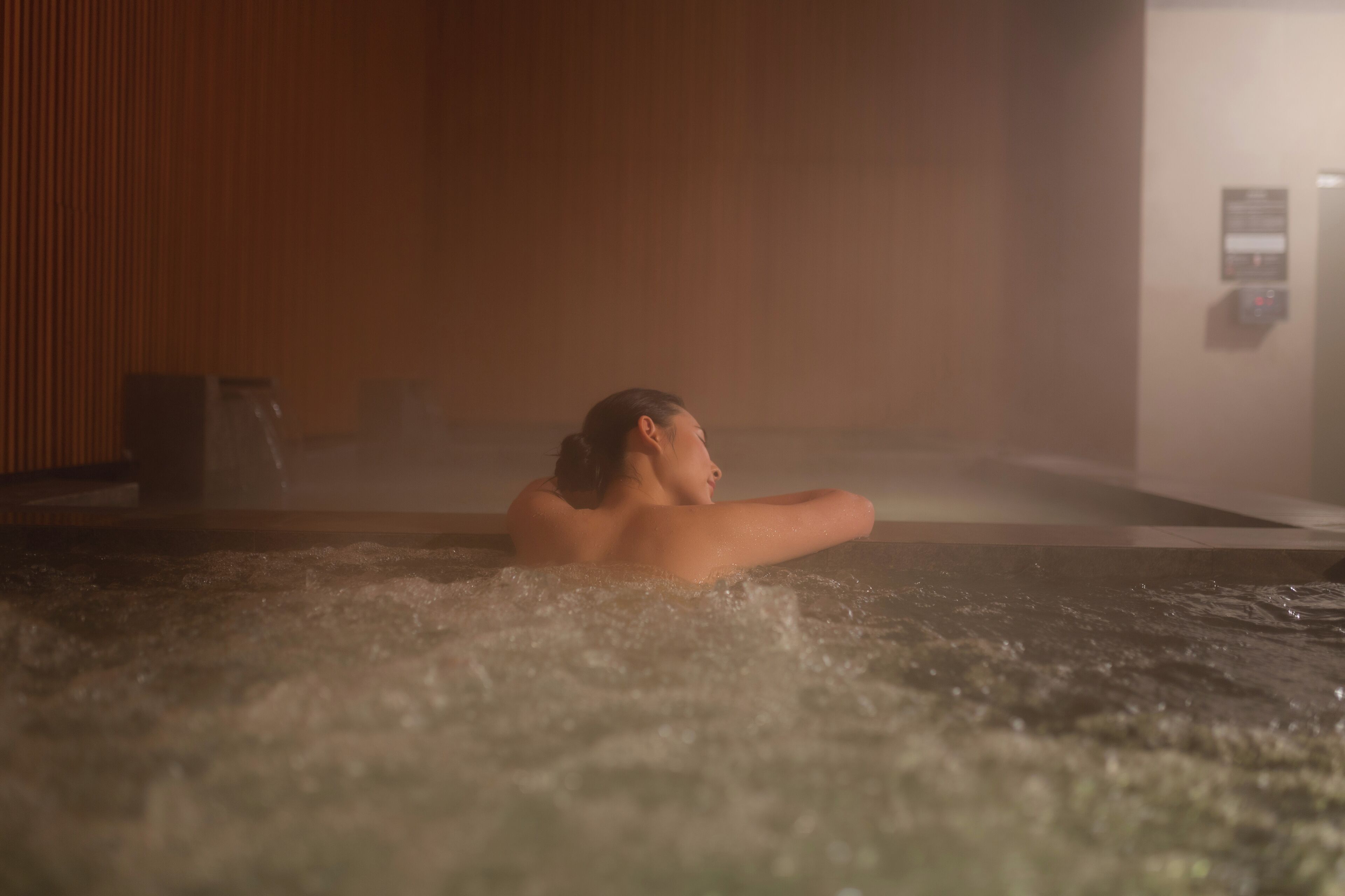Eine Person entspannt sich in einer Hot Tub vor einer Holzwand mit Bedienfeld im Hintergrund.
