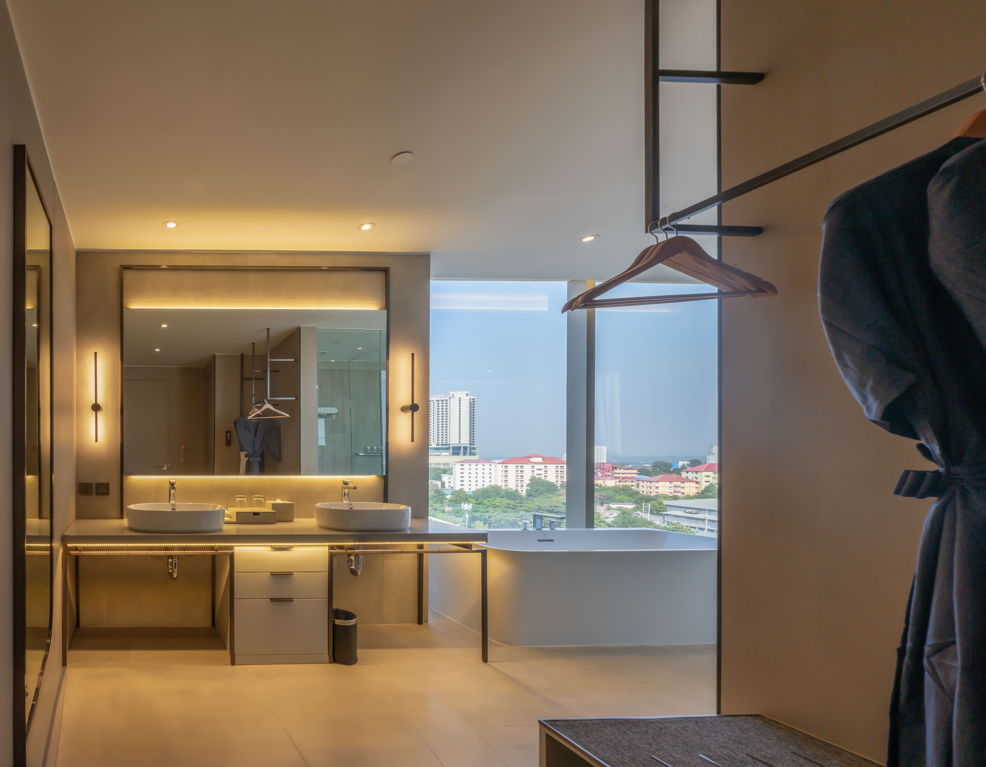 Un baño moderno con un espejo grande, lavamanos dobles y vistas a la ciudad a través de un ventanal amplio.