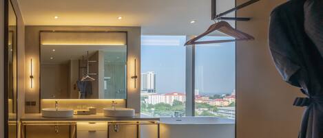 Un baño moderno con un espejo grande, lavamanos dobles y vistas a la ciudad a través de un ventanal amplio.