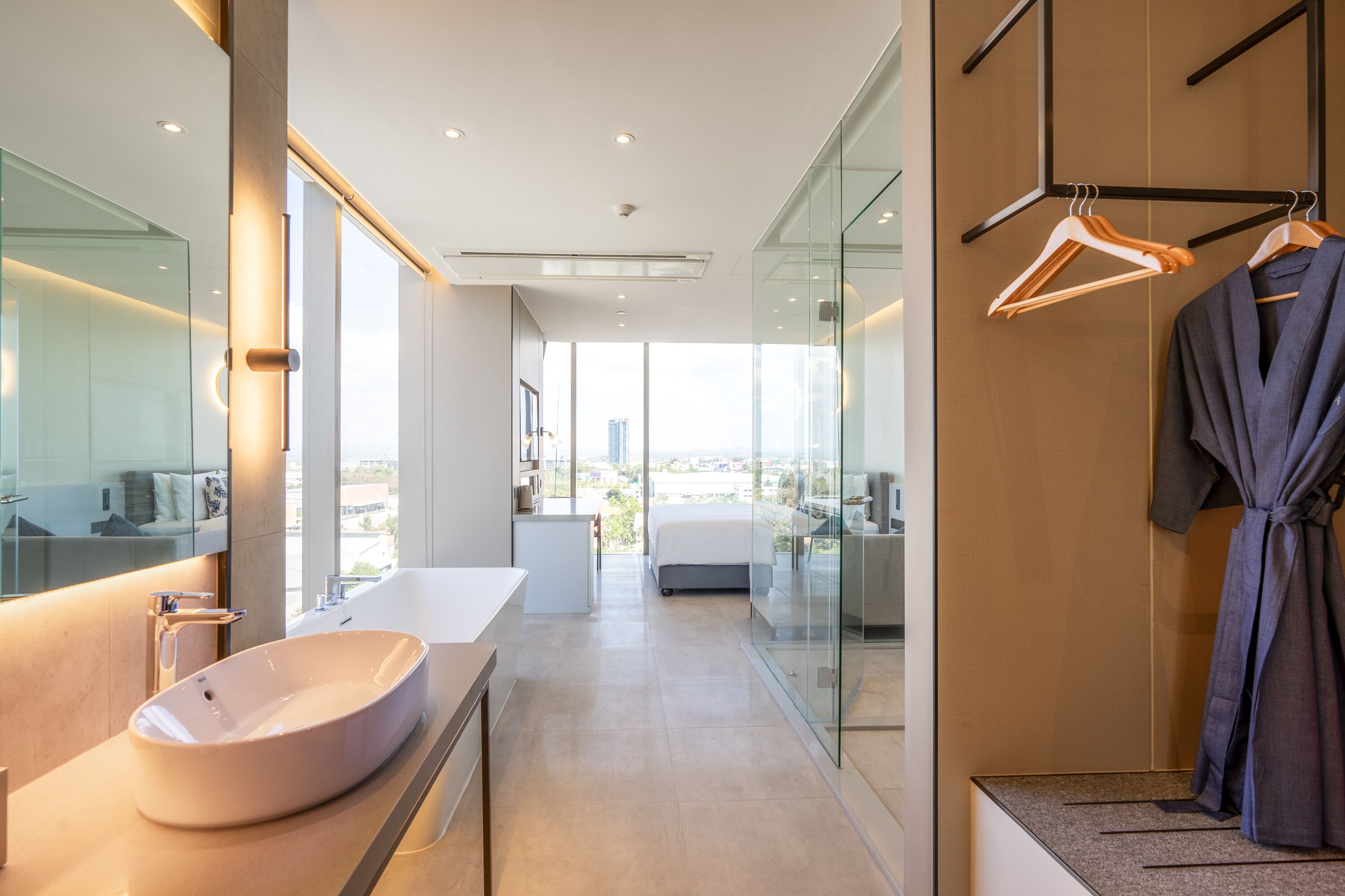 A modern hotel room with a large oval sink, a glass shower enclosure, and a view of the cityscape.