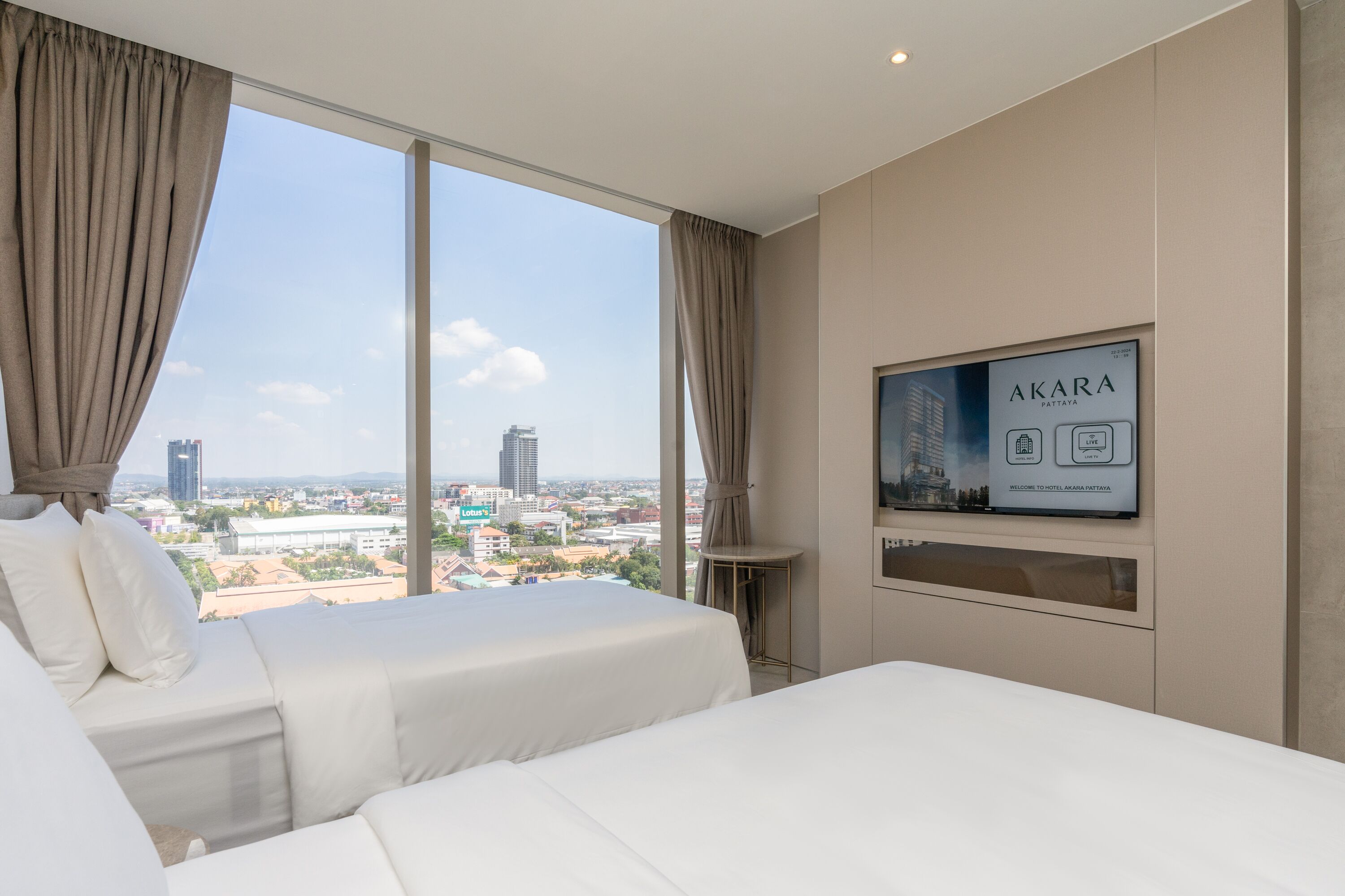A hotel room with two beds, a large window with curtains, a flat-screen TV on the wall, and a city view.