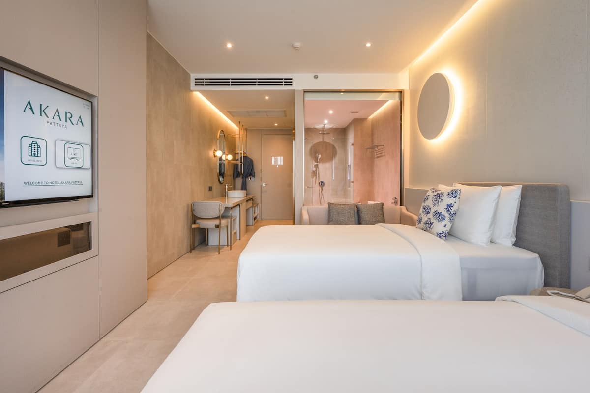 A modern hotel room with a bed, bedside table, and a mirror. There is a sign on the wall and a shower area visible in the background.