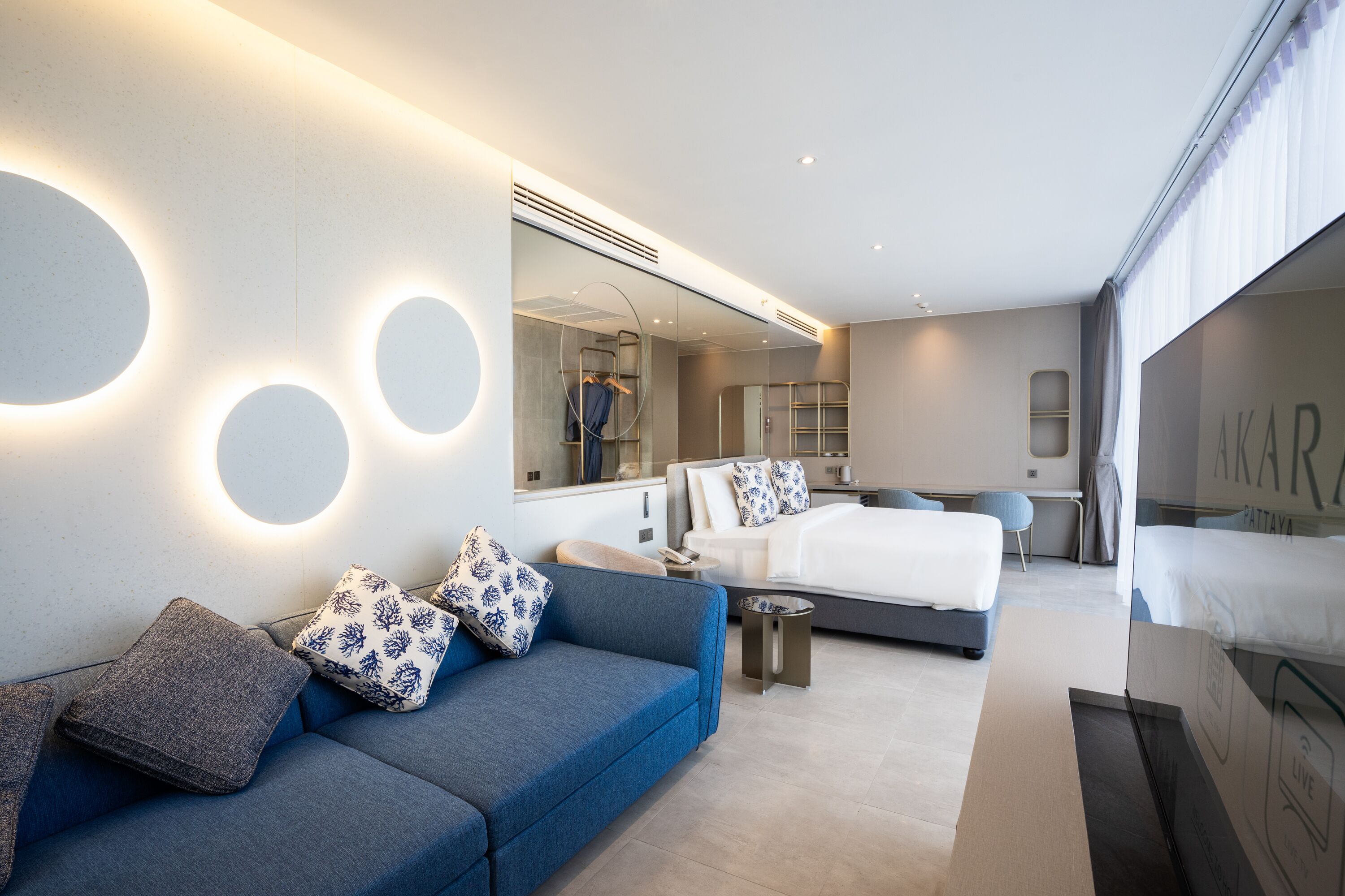 A modern hotel room with a blue sofa, a bed, a small table, and a mirror.