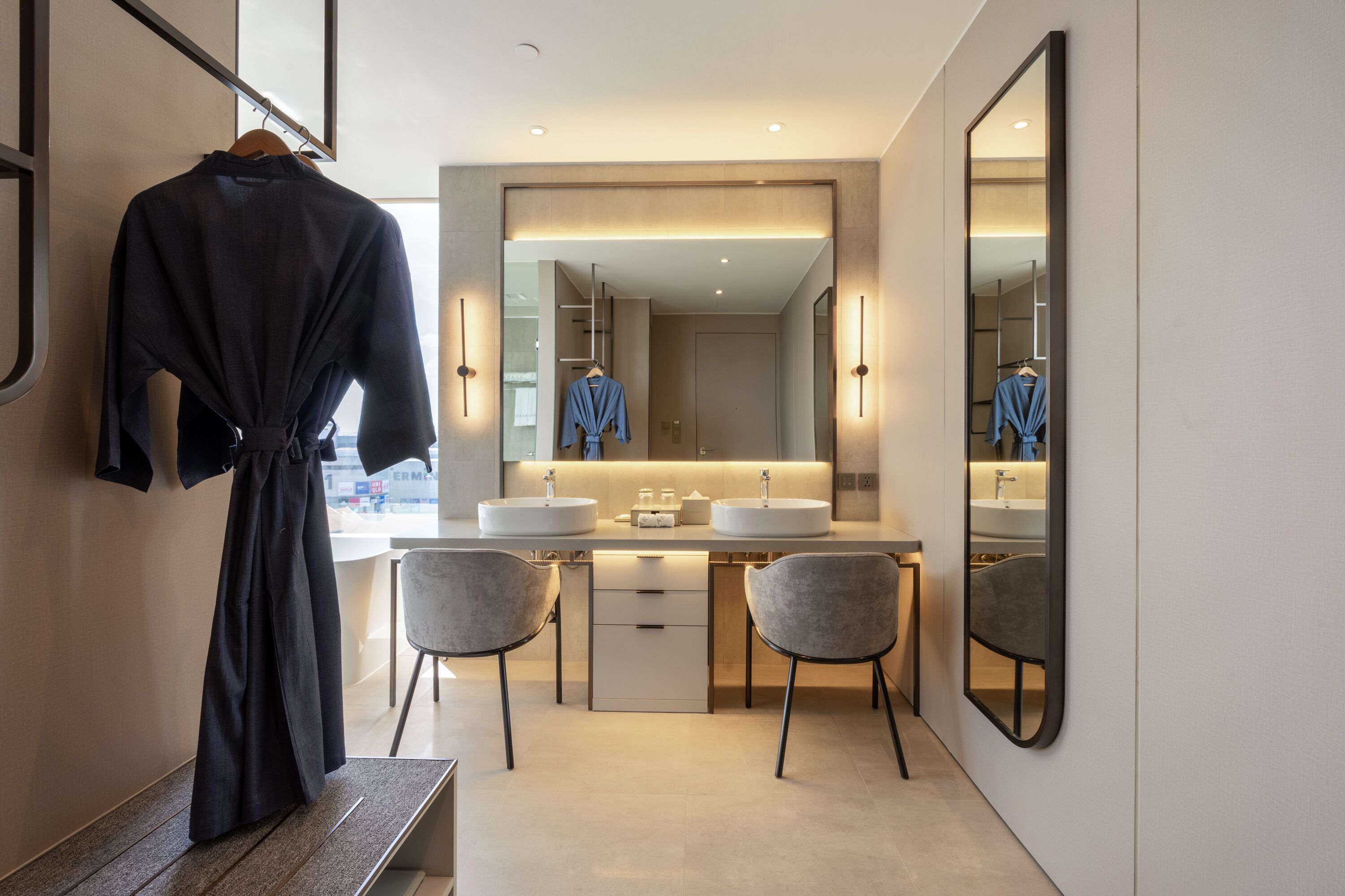 A modern bathroom with a large mirror, two sinks, and a robe hanging on a rack.