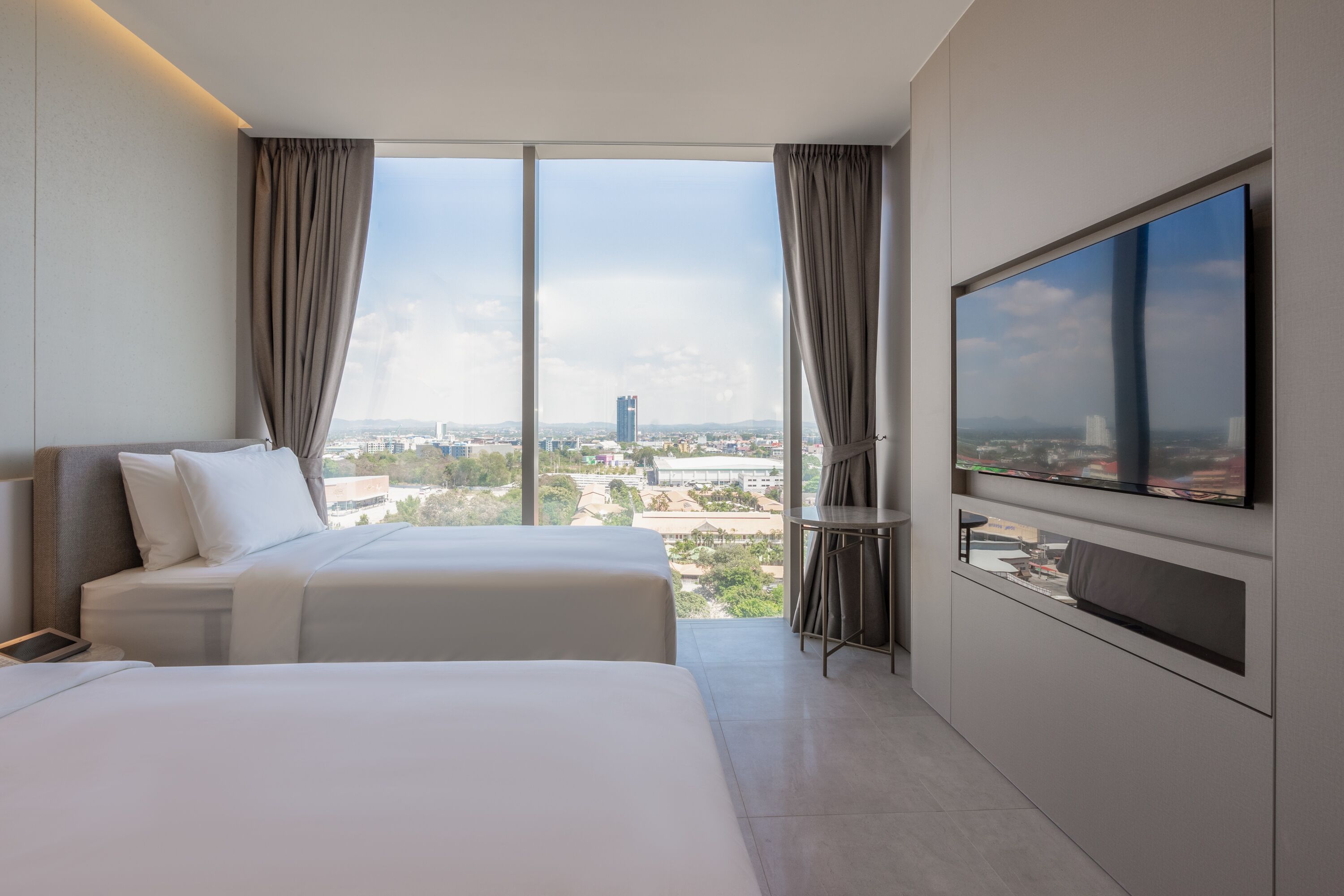 Une chambre d’hôtel avec deux lits, une grande télévision et une vue sur la ville.