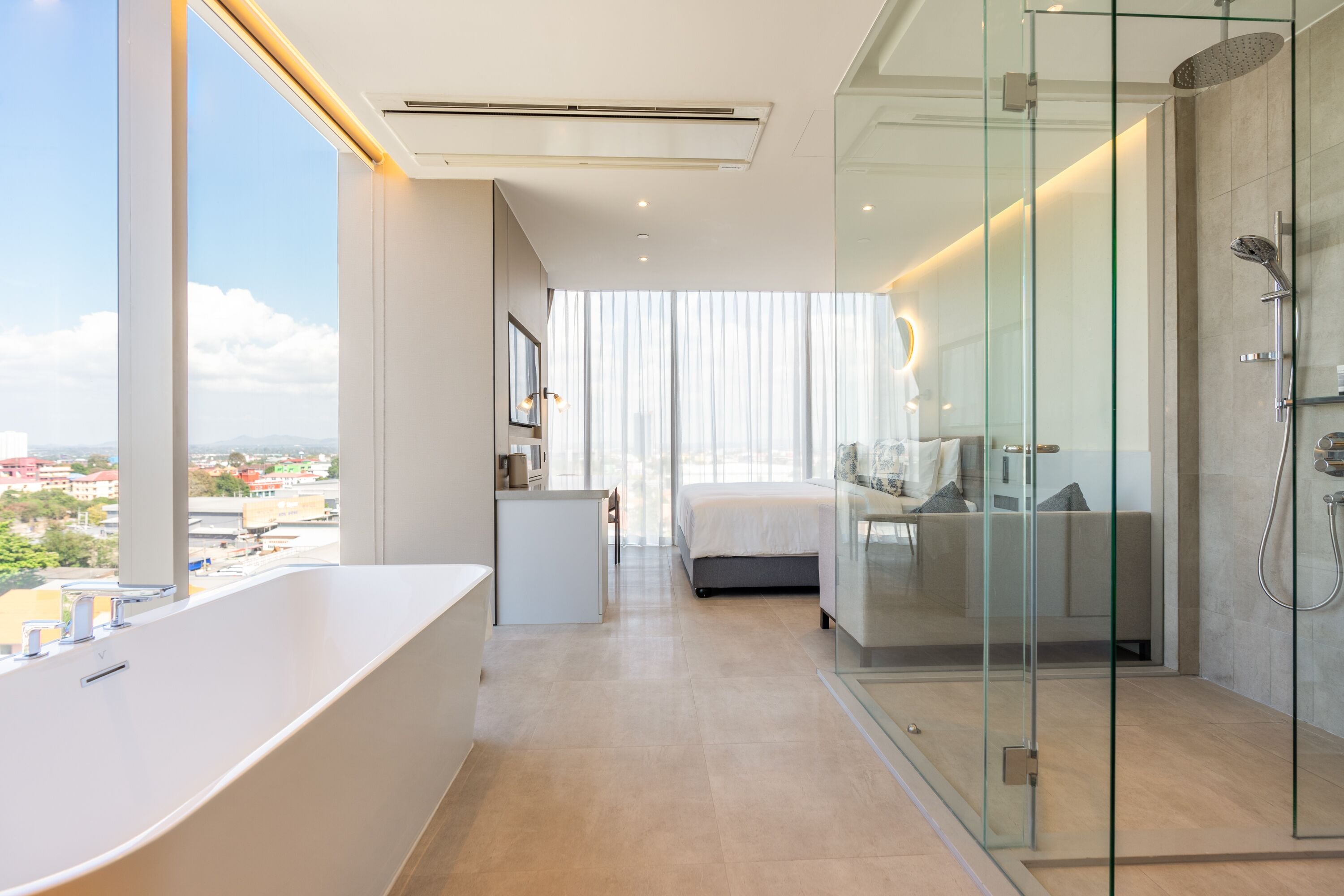 Ein modernes Hotelzimmer mit einer großen Badewanne, einer gläsernen Dusche und einem Bett mit Blick auf die Stadt.