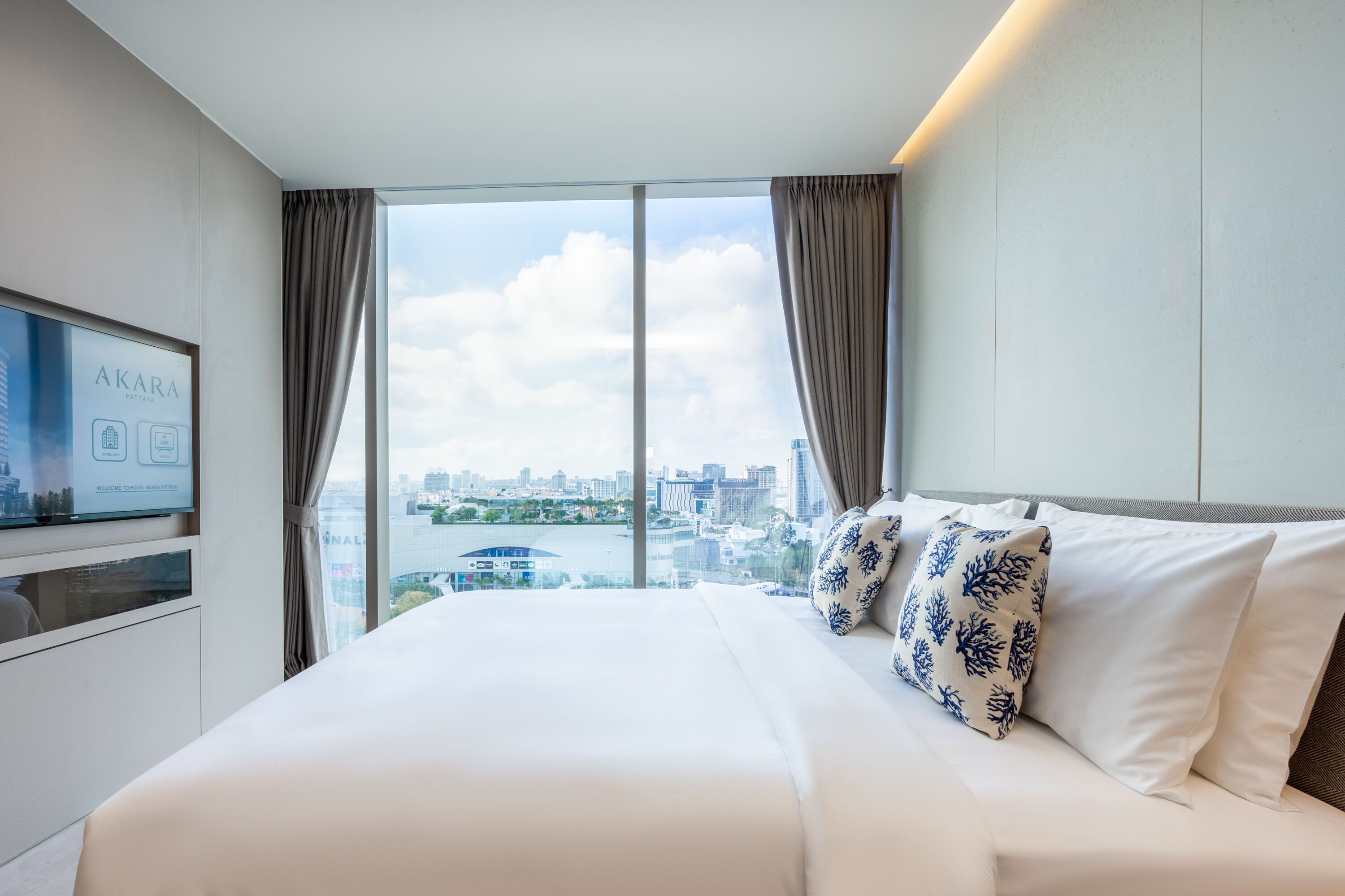 A hotel room with a large bed, a TV on the wall, and a city view through the window.
