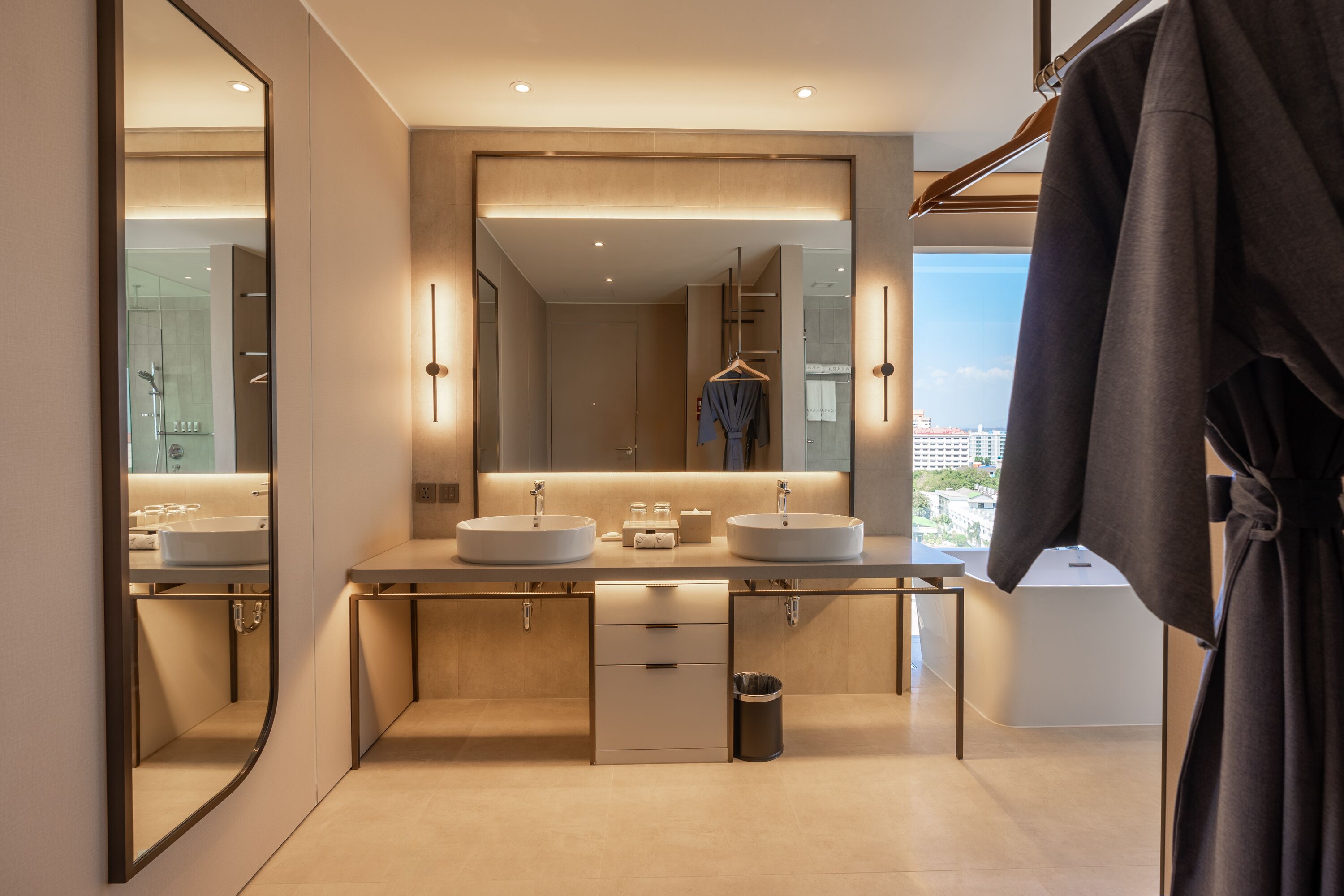 Un baño moderno con dos lavamanos, un espejo grande y vistas a la ciudad.