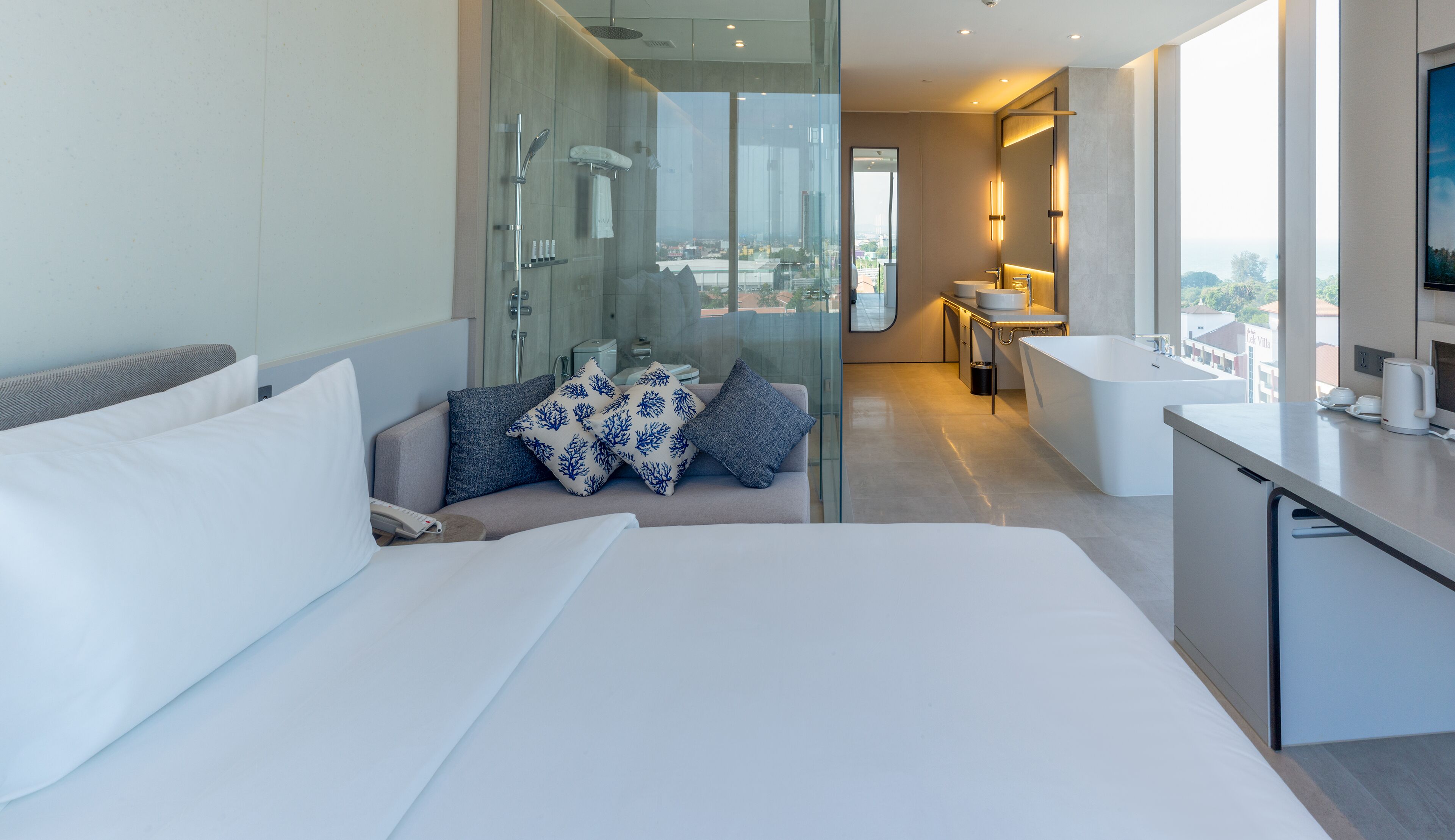 A modern hotel room with a large bed, a seating area with a view, a separate bathroom, and a kitchenette.