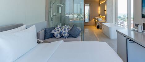 A modern hotel room with a large bed, a seating area with a view, a separate bathroom, and a kitchenette.