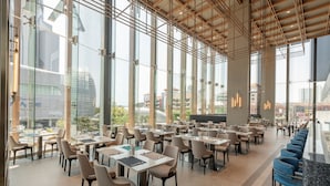 Un vaste espace intérieur doté de nombreuses tables et chaises, de grandes fenêtres et d’un haut plafond laissant apparaître les poutres apparentes.