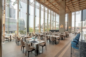 A spacious indoor area with multiple tables and chairs, large windows, and a high ceiling with visible structural beams. - Akara Hotel Pattaya (Pattaya)