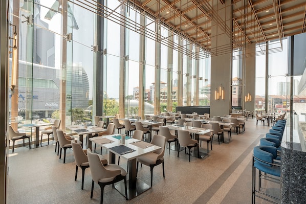 A spacious indoor area with multiple tables and chairs, large windows, and a high ceiling with visible structural beams. - Akara Hotel Pattaya (Pattaya)