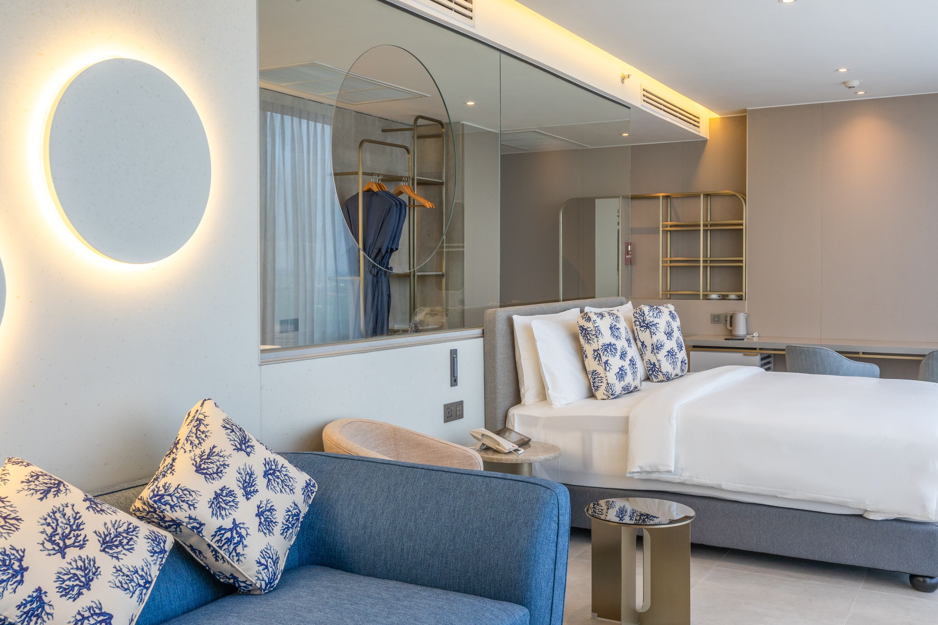 A modern hotel room with a large bed, a sofa, a small table, and a mirror.