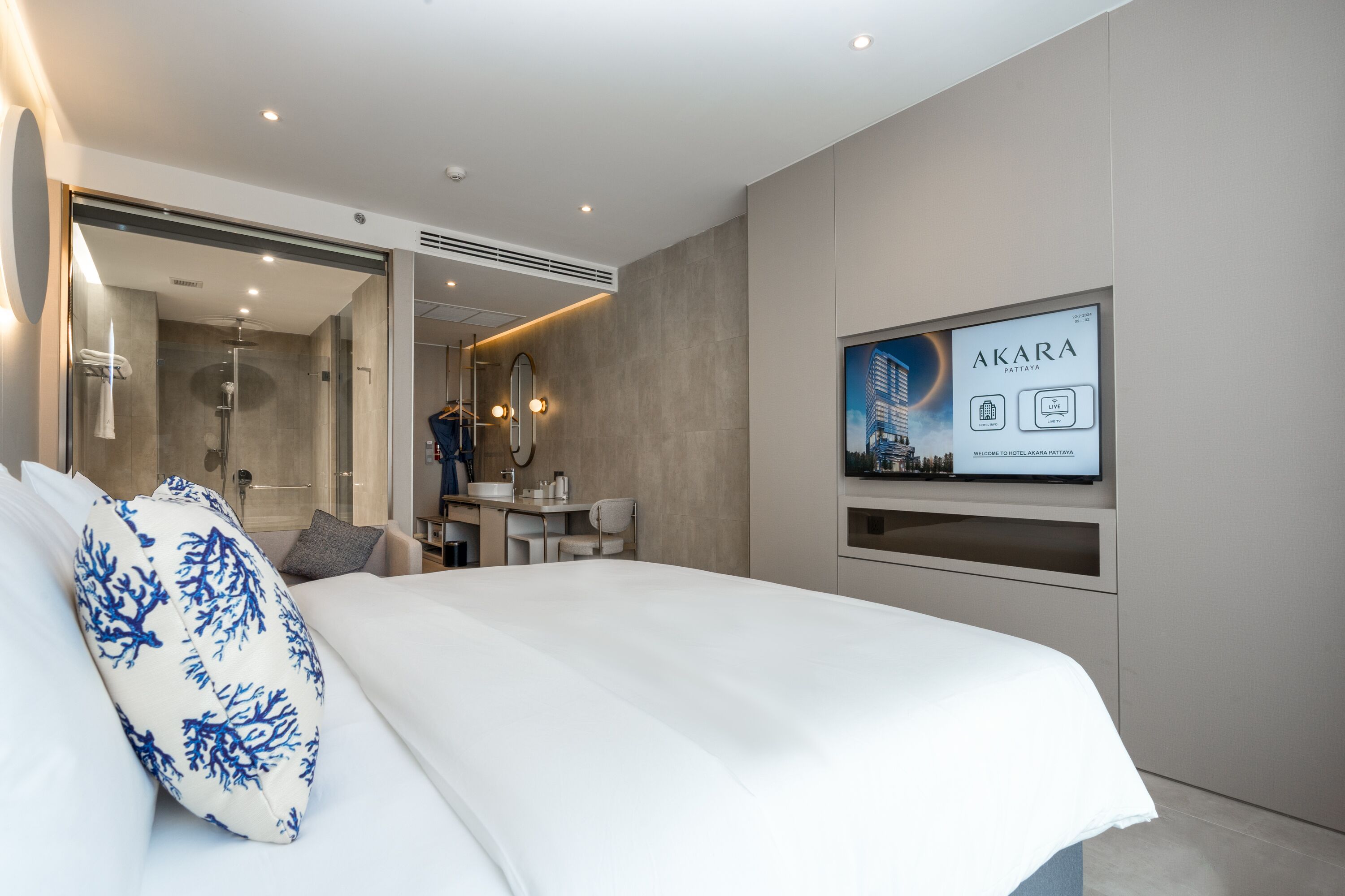 Una habitación de hotel moderna con una cama grande, un baño con ducha y un televisor mostrando el nombre del hotel.